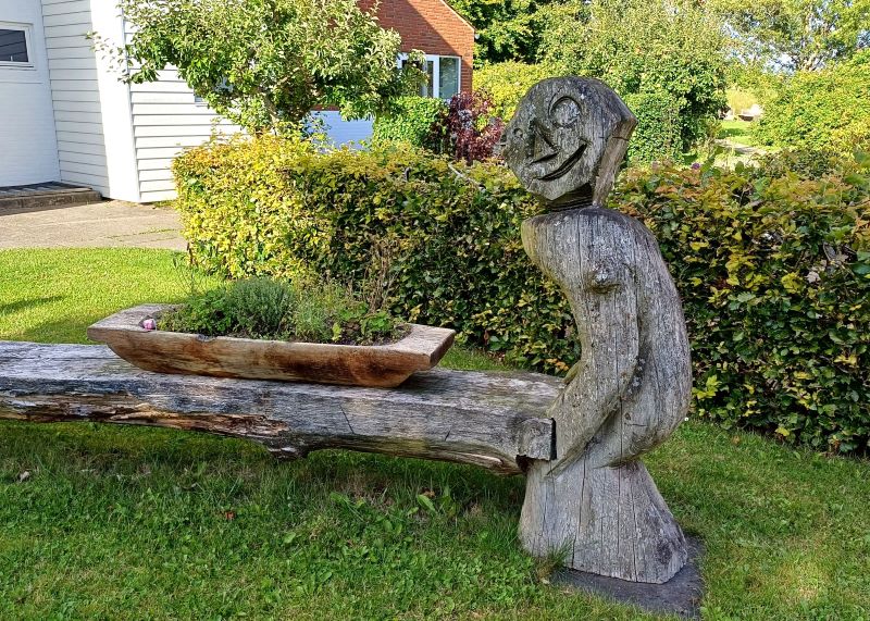 Billede af træfigur som udgør den ene ende af en bænk. Skåret med kædesav af bofællesskabets mandlige beboere.