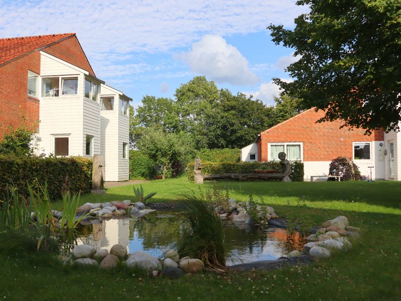 Billedet fra stedet viser et udsnit af vores fælles plæne med dam og to huse i baggrunden